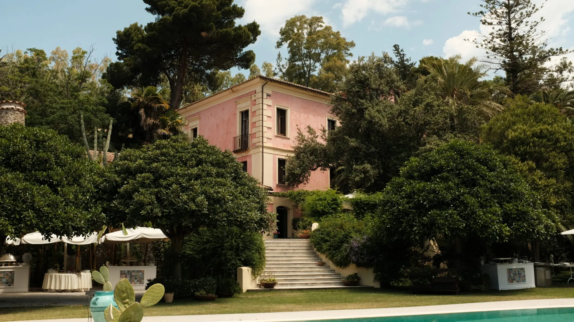 La facciata rosa di Villa Ventura tra gli alberi e la piscina