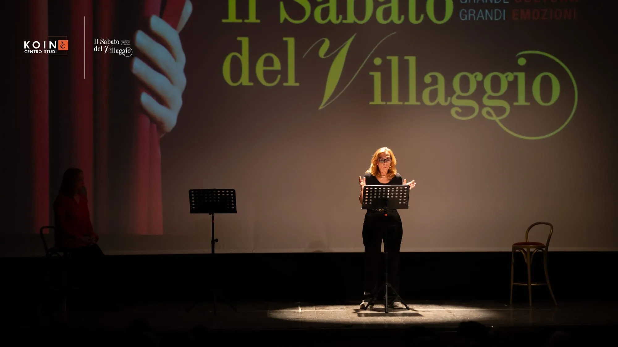 Una lettura sul palco con il logo del Sabato del Villaggio sullo sfondo